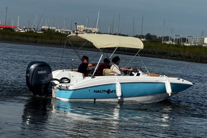 Small motorboat with canopy and three people on a calm river near the shore.
