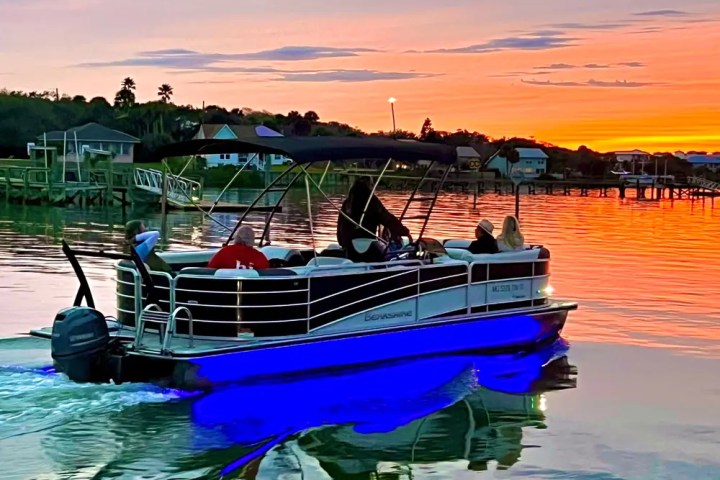 Pontoon boat on a lake at sunset with blue lights reflecting on water.