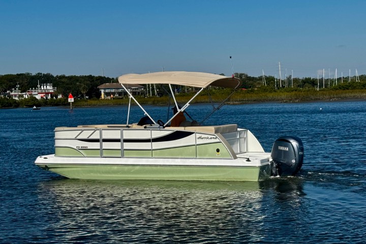 Side view of a pontoon boat with canopy on a calm lake.