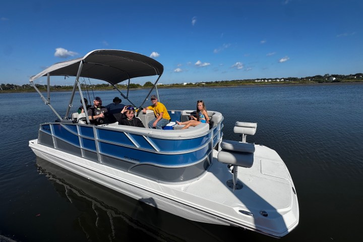 Group on a blue pontoon boat under a canopy on a sunny day.