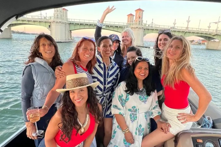 Group of women smiling on a boat with a bridge in the background.