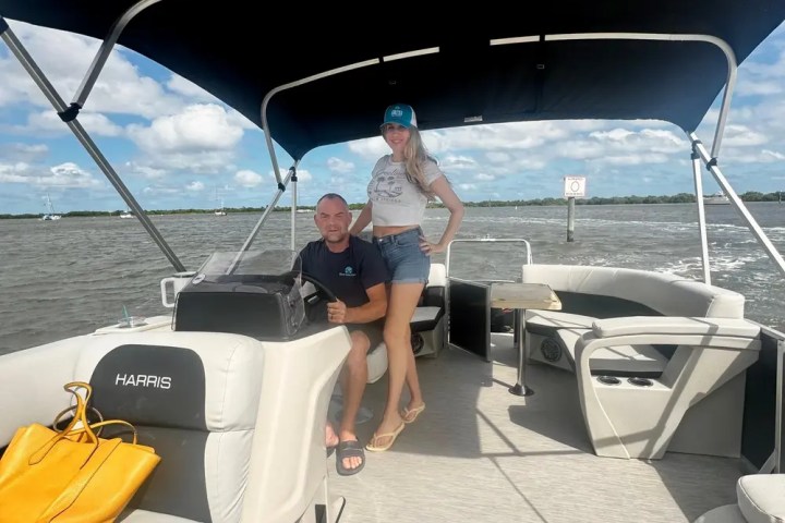 Two people on a boat under a canopy, with a yellow bag on the seat.
