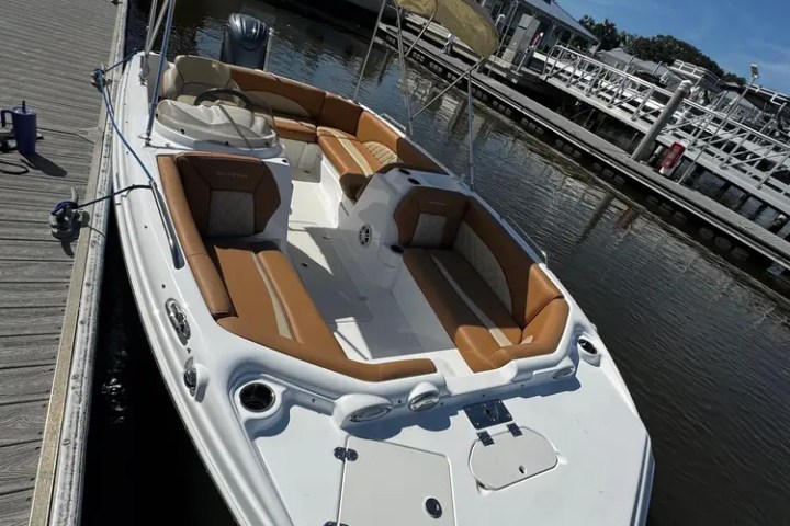 White motorboat with tan seats docked at a marina under a clear blue sky.