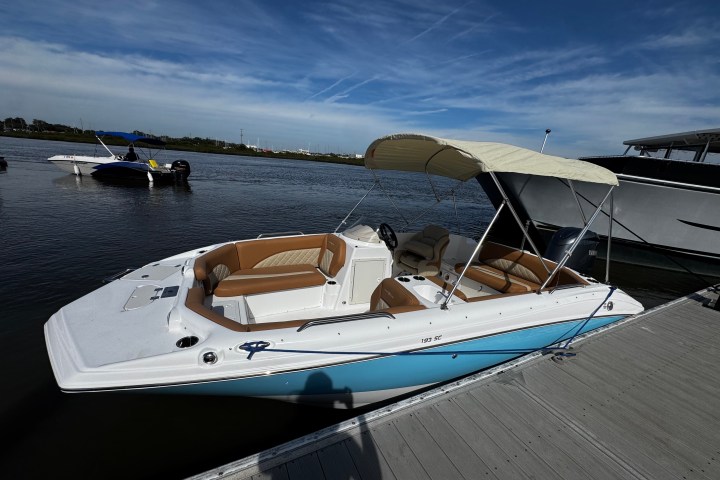 Small white motorboat with tan seats docked by a pier under blue sky.