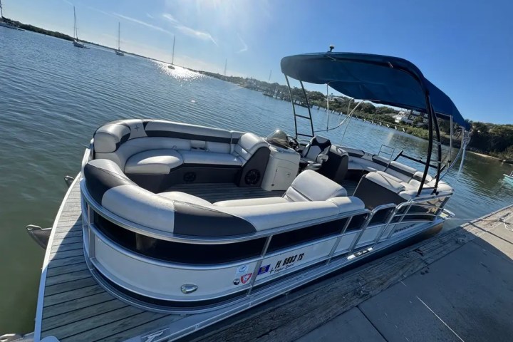 Pontoon boat docked on a calm lake under a clear blue sky.
