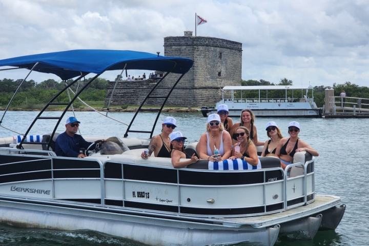 Group on a pontoon boat near a stone fort by the water, with cloudy skies overhead.