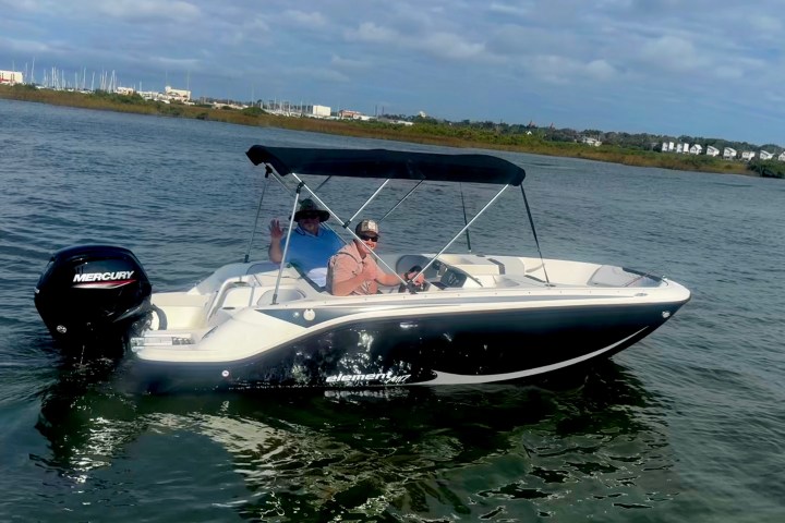 Two people on a motorboat with a canopy cruising on calm waters.