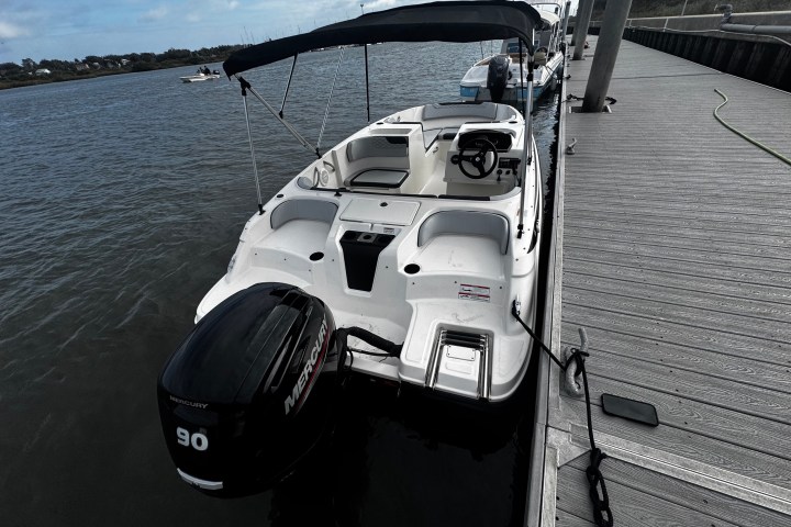 White motorboat docked at a wooden pier on a calm river.