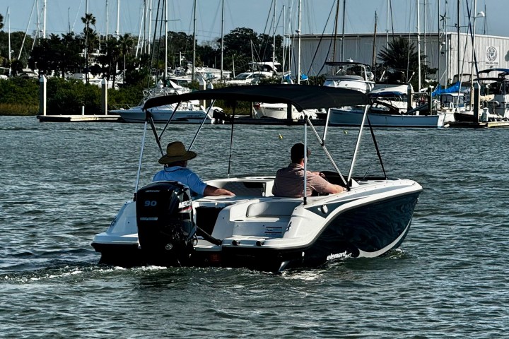 Two people on a small motorboat with a canopy in a marina.