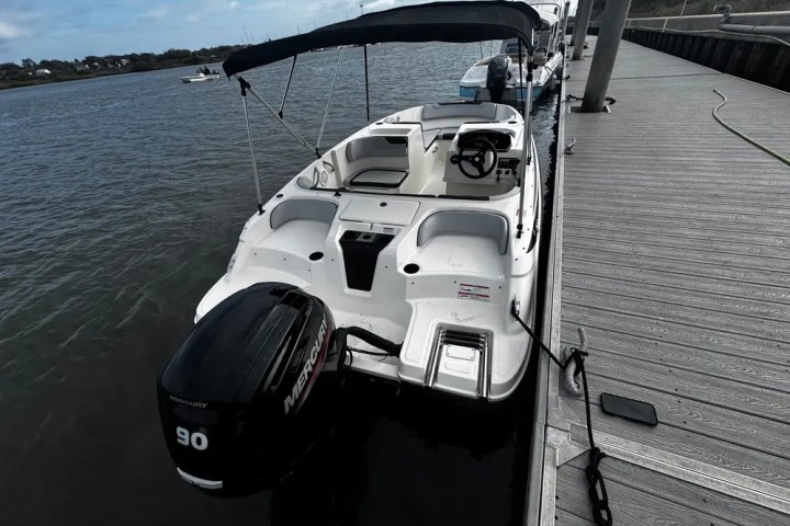 White motorboat with canopy docked beside a wooden pier.