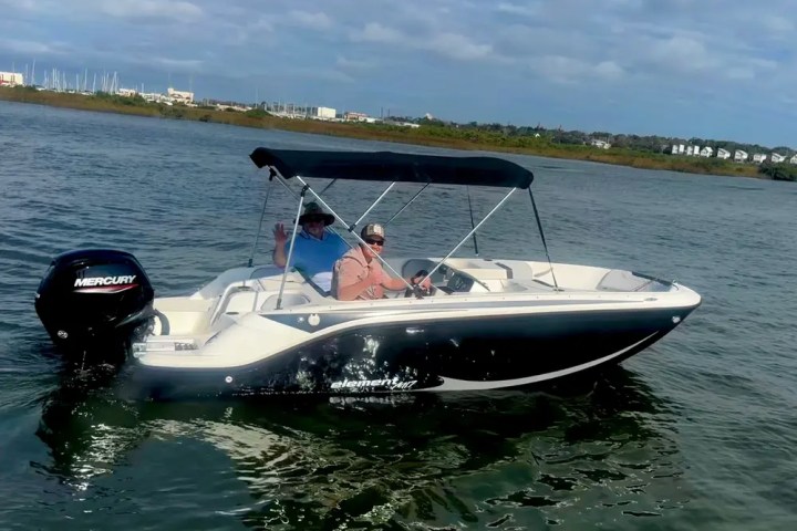 Two people in a small motorboat on a calm body of water under a cloudy sky.