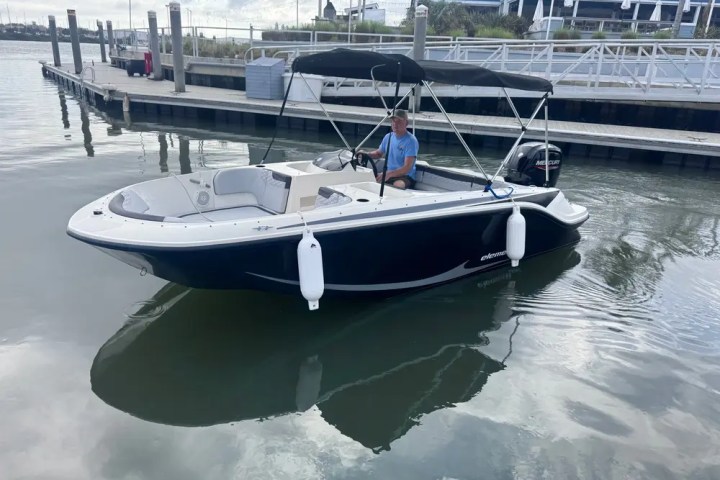 Person in a small motorboat with a canopy on calm water next to a dock.