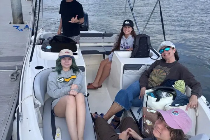 Five people relaxing on a small boat docked at a river with cloudy skies.