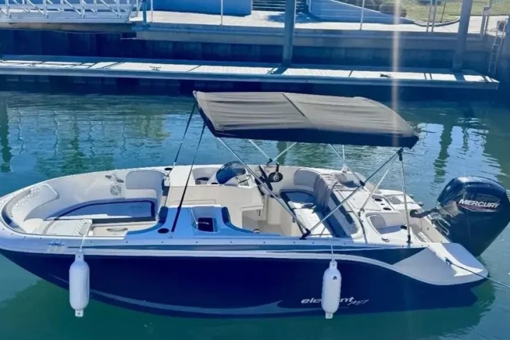 Small motorboat with canopy docked in a marina with clear water.