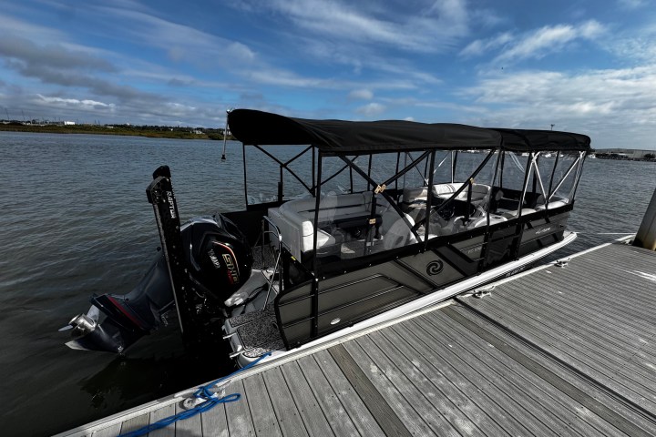 Covered boat docked at a pier with a scenic background of water and sky.