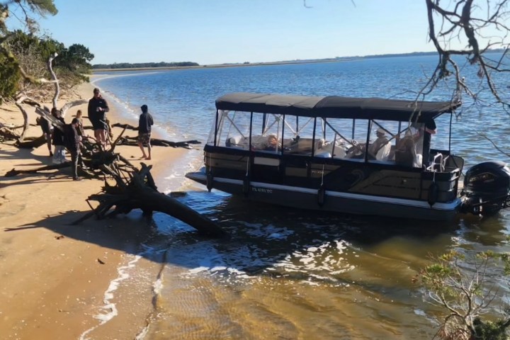 People stand on a sandy shore with a small boat docked beside them.