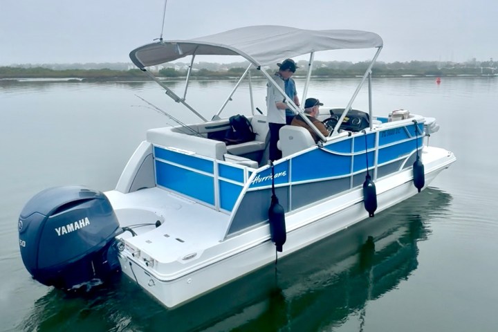 Two people on a blue pontoon boat with a canopy, floating on calm water.