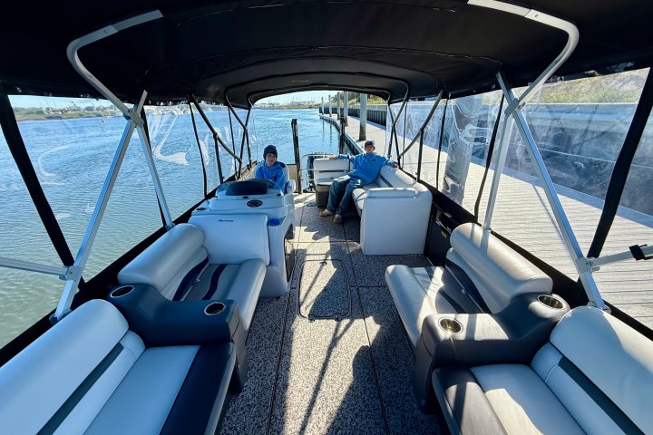 Interior of a pontoon boat with two people seated, moored by a dock, under a black canopy.
