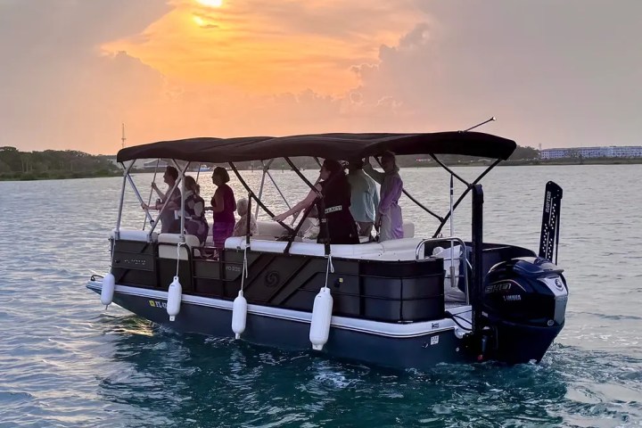 People on a pontoon boat at sunset on calm water.