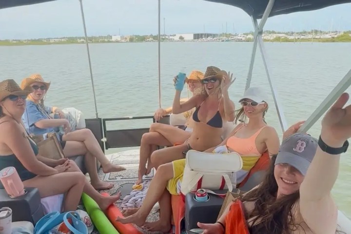 Group of people relaxing on a boat with drinks and hats.
