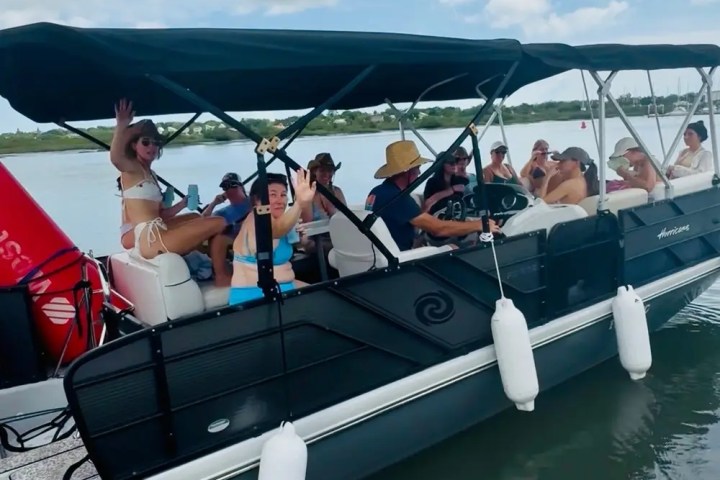Group of people on a pontoon boat by a dock under a blue sky with clouds.