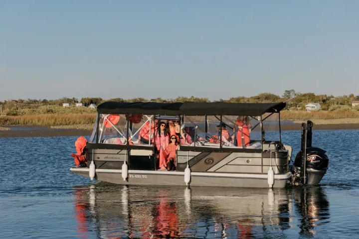 Pontoon boat on water with people in red life jackets.