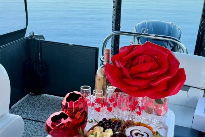 Elegant charcuterie spread on a boat with red rose and glasses, lakeside view.