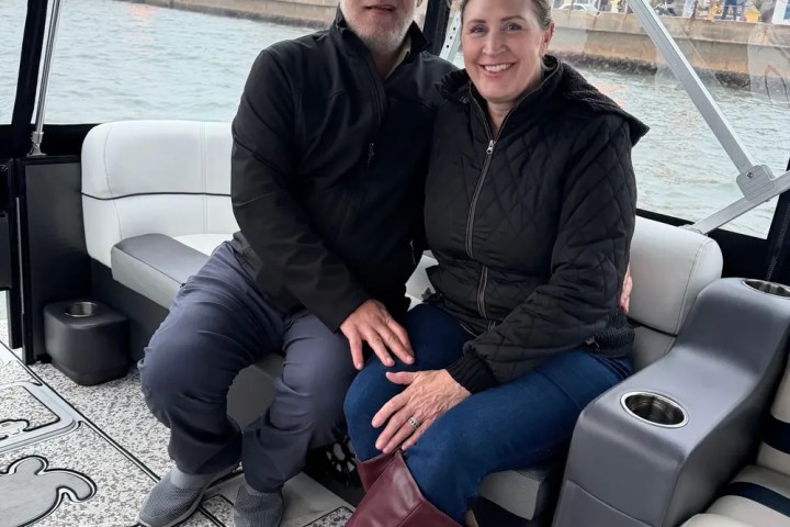 Couple sitting on a boat with water and cityscape in background.