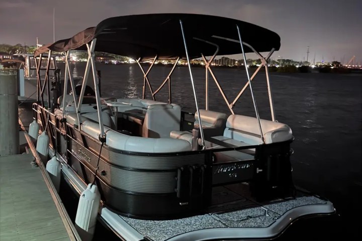 Pontoon boat docked at night with city lights in the distance.