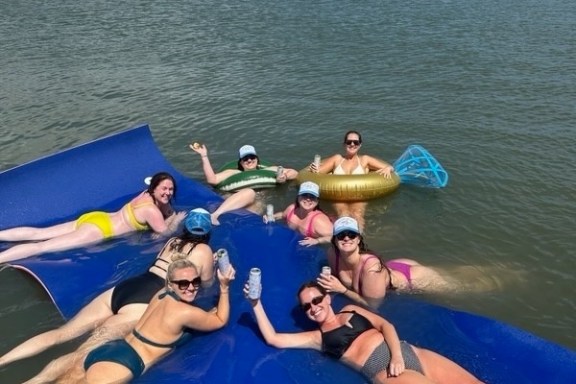 Group of women relaxing on a blue floating mat in a sunny lake.