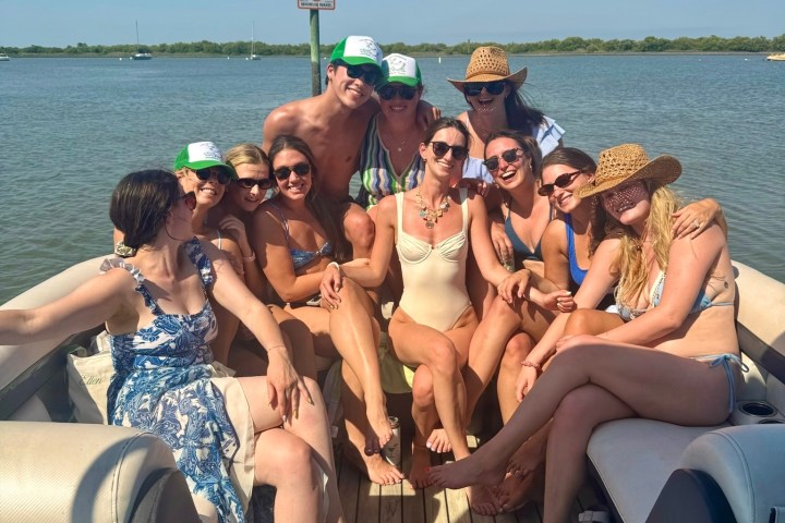 Group of people on a boat enjoying a sunny day, wearing summer attire and hats on a lake.