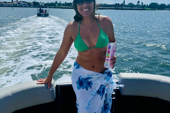 Smiling person on a boat wearing a captain's hat and green bikini with a floral wrap.