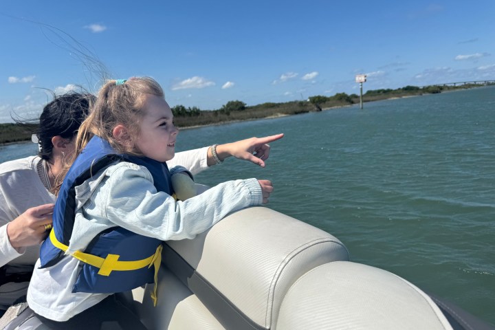 Child in a life jacket pointing while sitting on a boat.