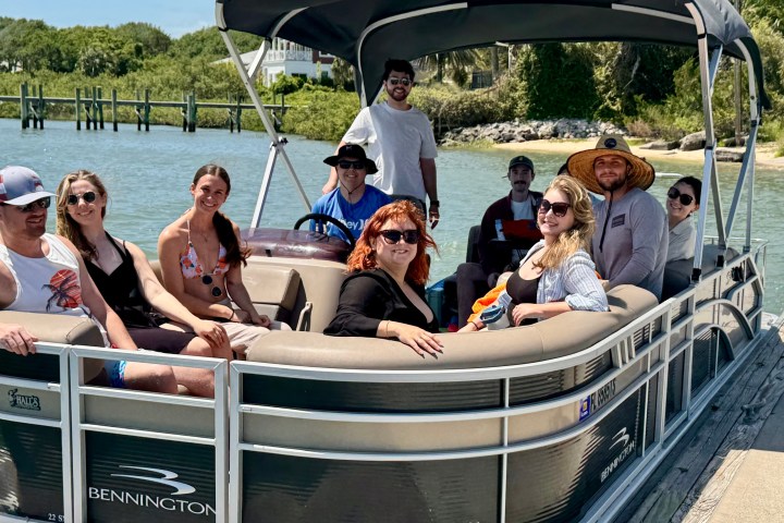 Group of people on a pontoon boat in a sunny, waterfront setting.