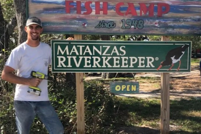 Man standing beside signs for Genung's Fish Camp and Matanzas Riverkeeper.
