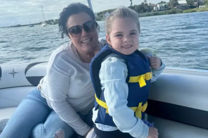 Woman and child in life jacket sitting on a boat on a sunny day.