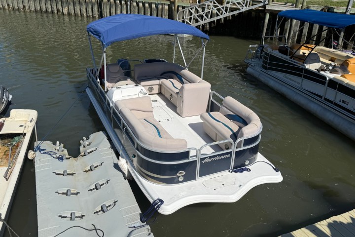 Pontoon boat docked, blue canopy, beige seats, near wooden pier.