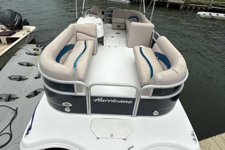 Docked pontoon boat with seating, canopy, and visible shoreline.