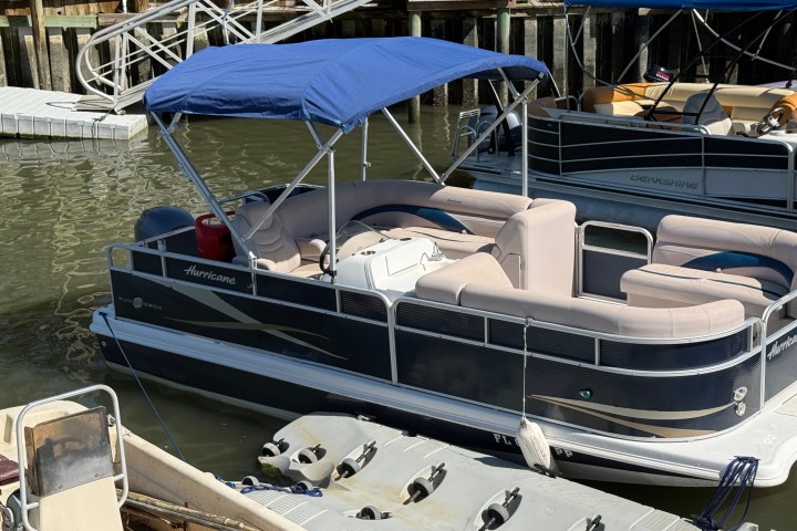 A pontoon boat with a blue canopy docked at a wooden pier.