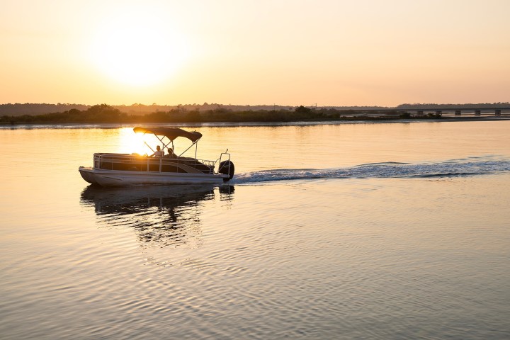 Boat cruising on a calm river at sunset with a bridge in the background.
