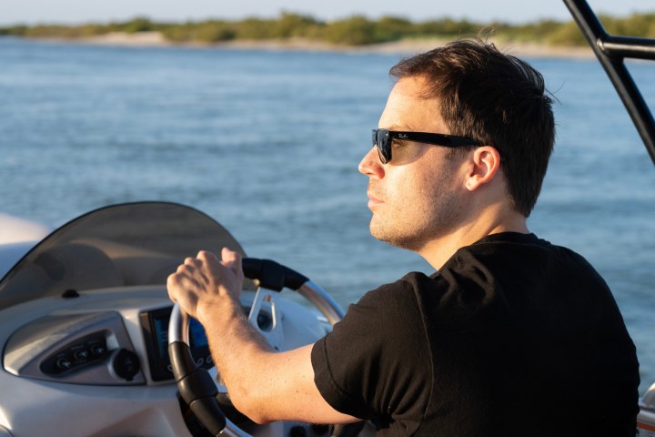 Person wearing sunglasses driving a boat on a sunny day.