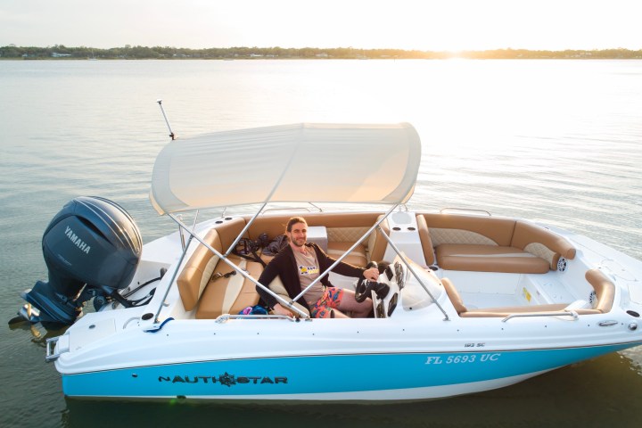 Person with a dog on a boat in calm waters at sunset.